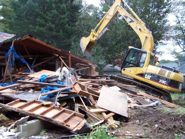 A yellow cat excavator is demolishing a house