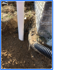A black pipe is laying in the dirt next to a white pole.