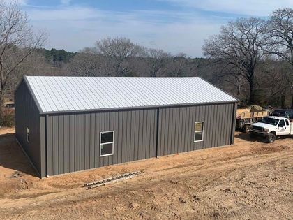 A large metal building with a white roof is sitting in the middle of a dirt field.