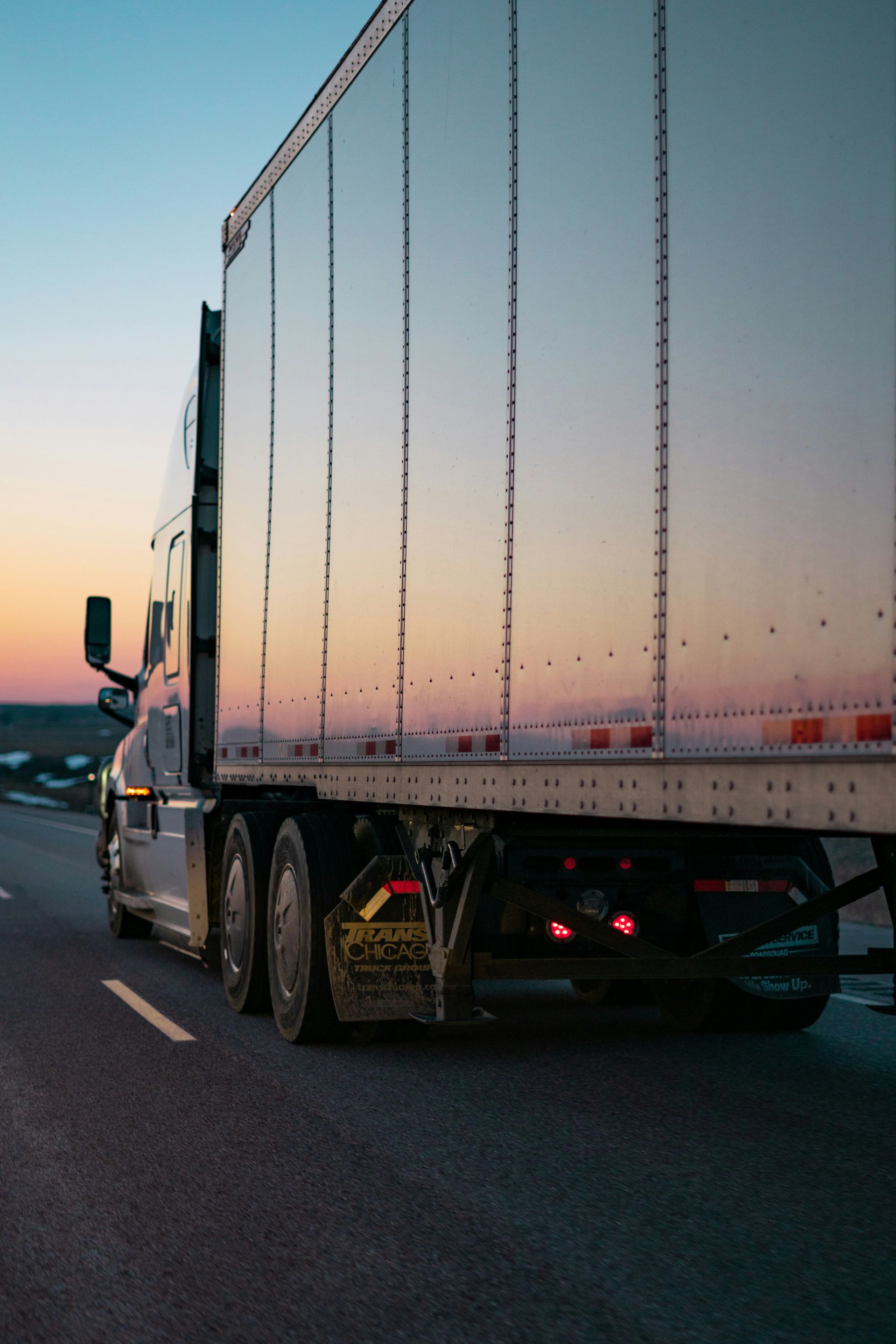 White semi-truck driving on a highway at sunset, viewed from behind