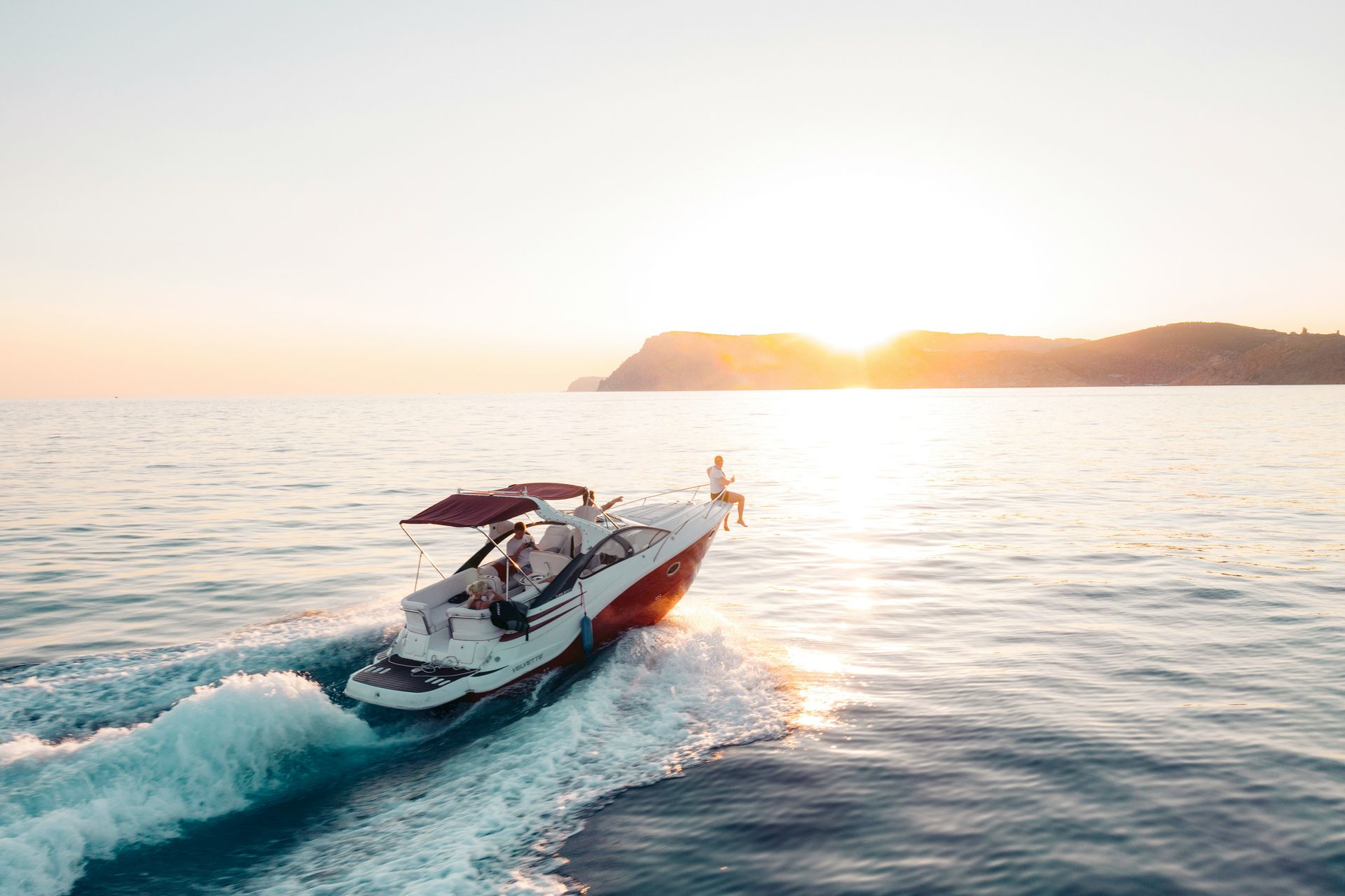 Speedboat cutting through calm ocean at sunset near a distant shoreline