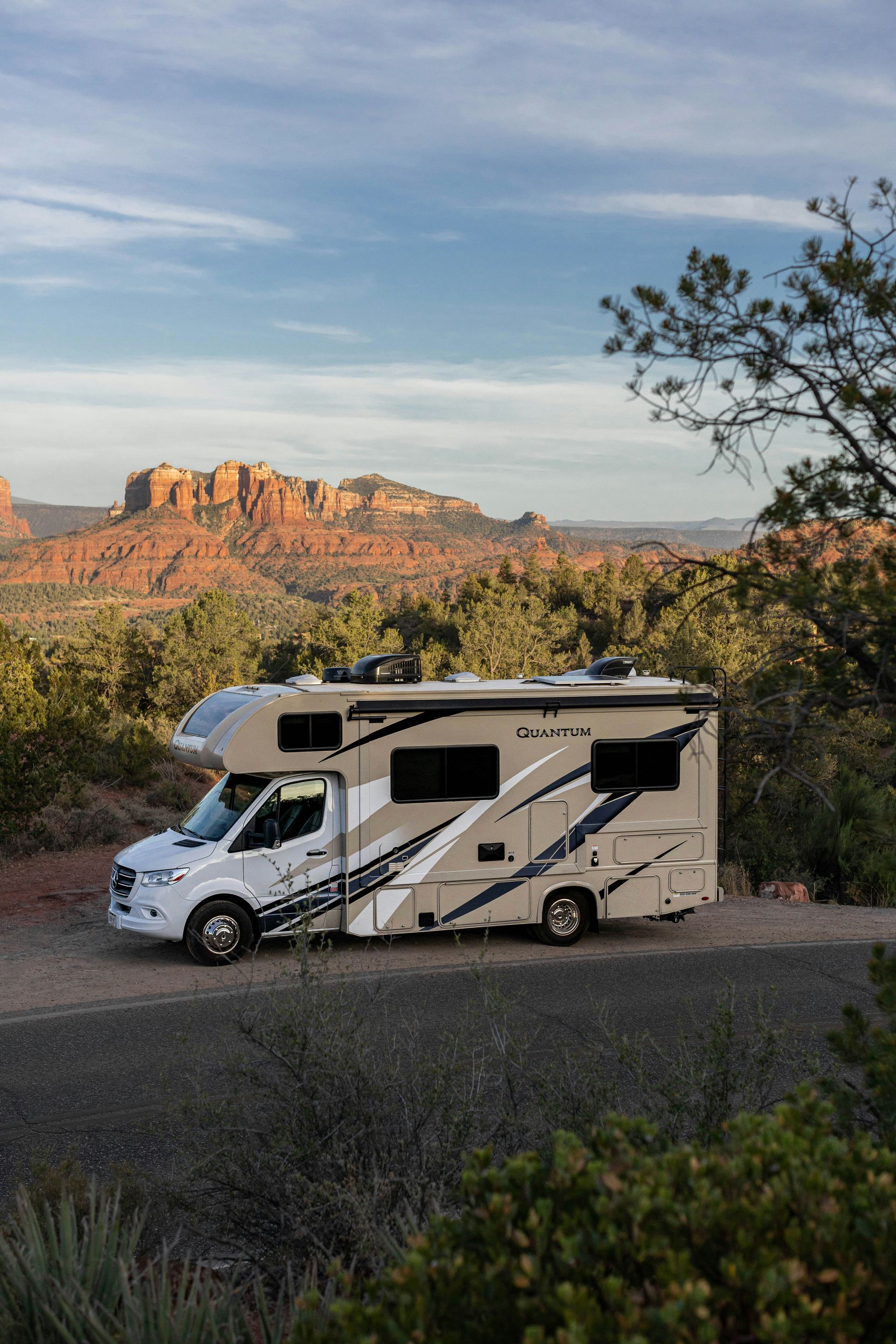 White RV parked on a desert overlook with red rock cliffs and blue sky in the background