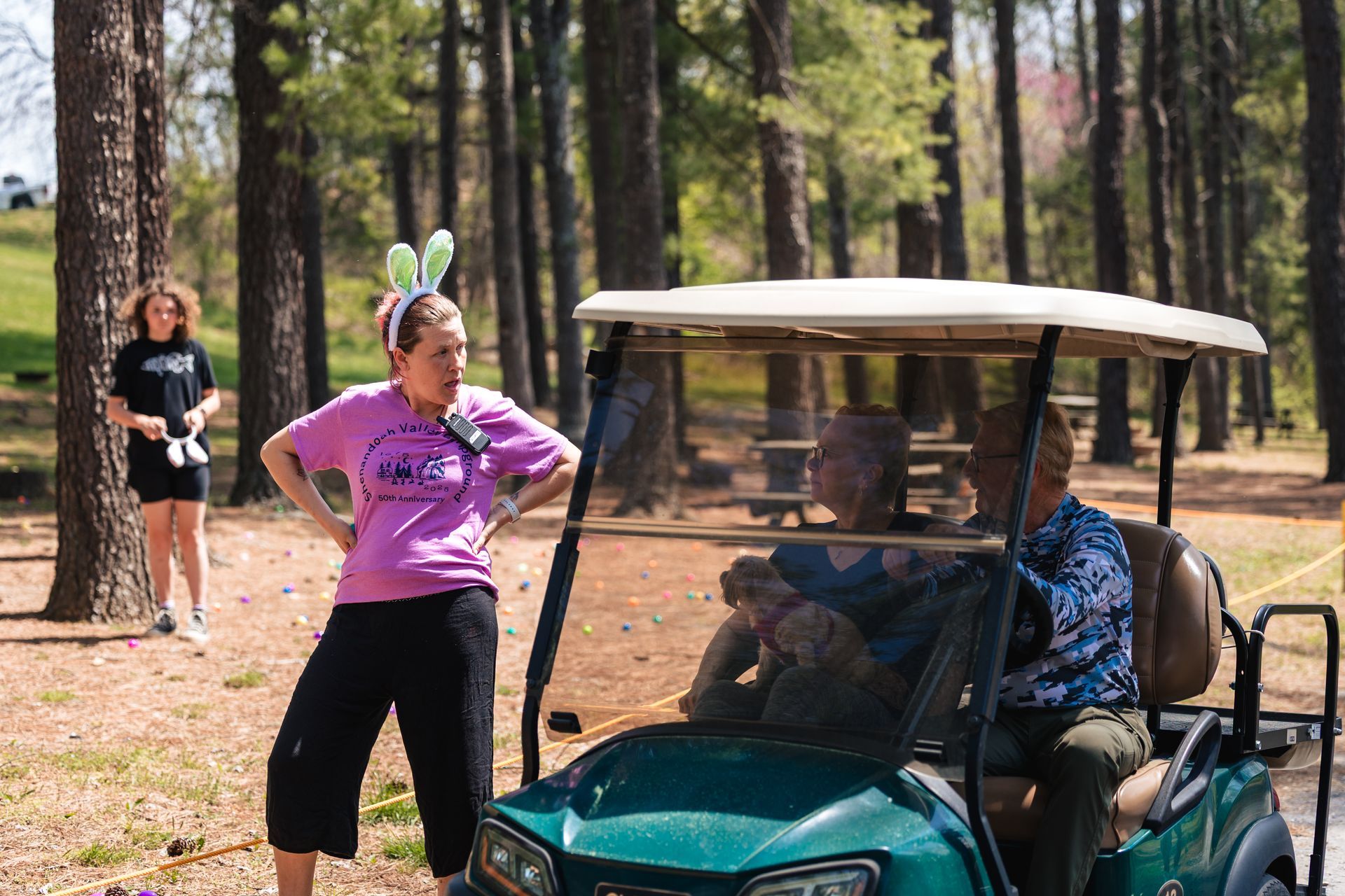 A woman wearing bunny ears is standing next to a golf cart.
