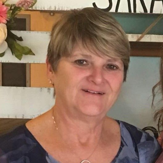 A woman wearing a blue shirt and a necklace smiles for the camera