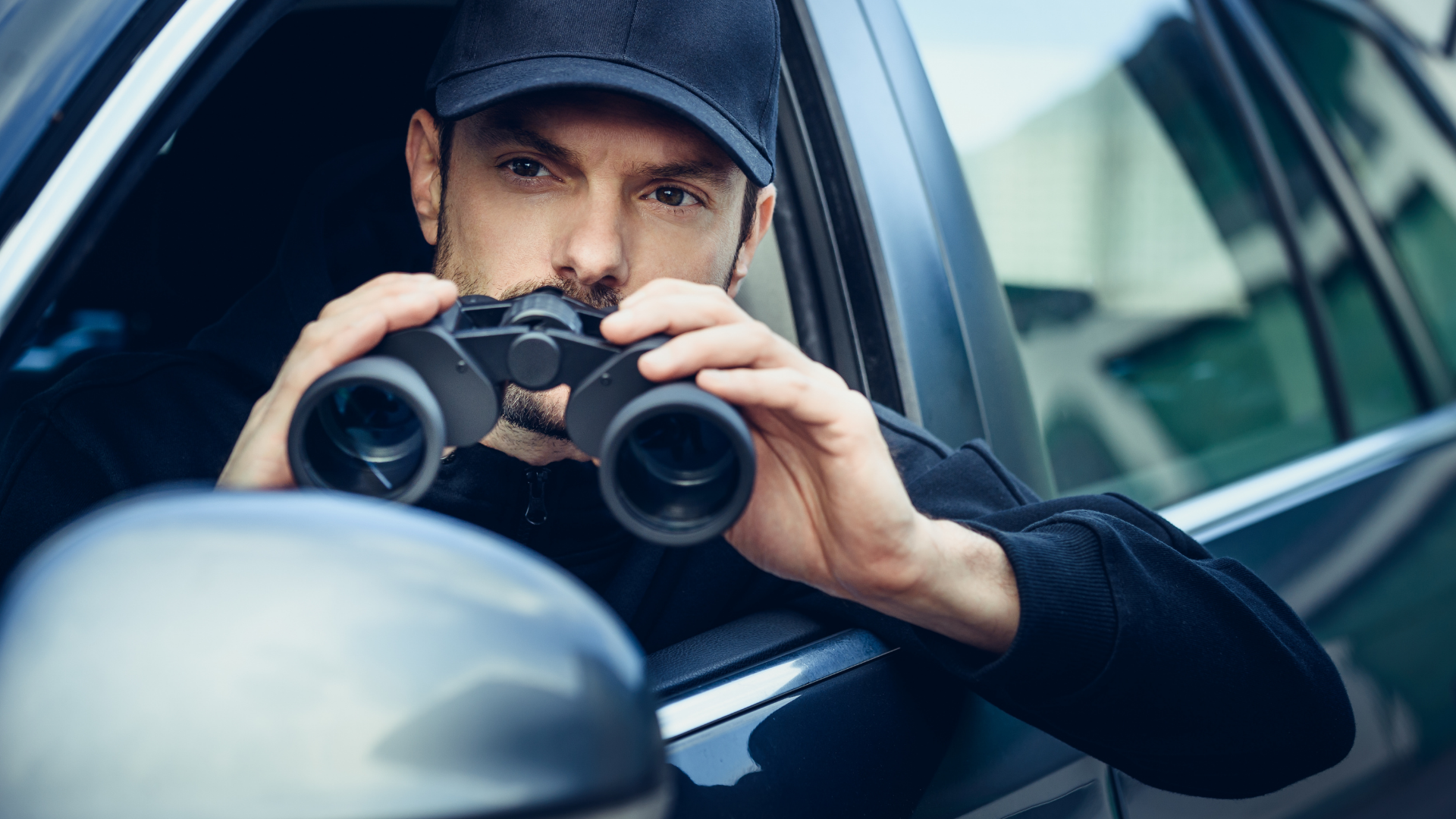 A man is sitting in a car looking through binoculars.