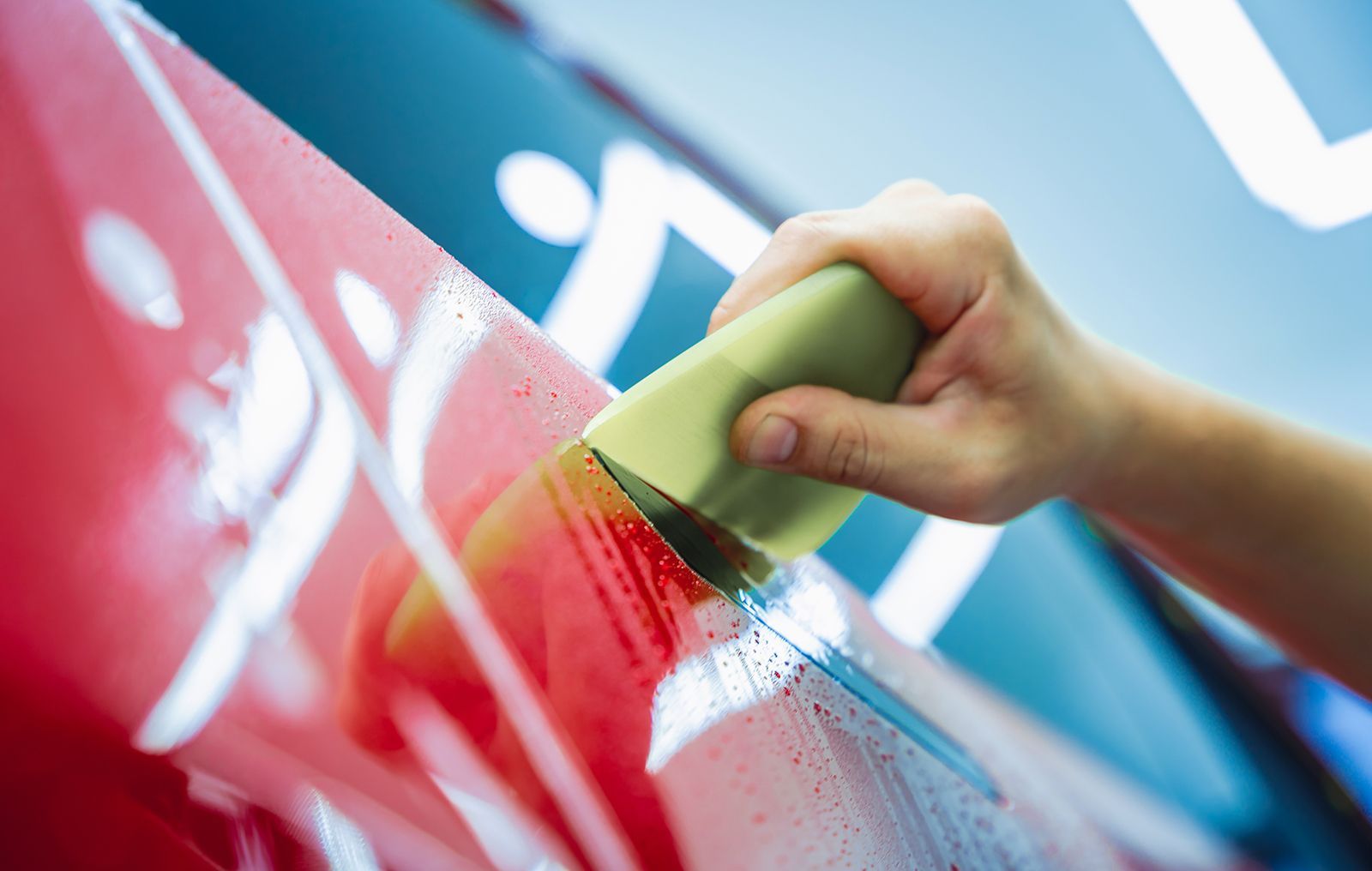 Mano utilizando una escobilla de goma sobre la carrocería del coche de color rojo, aplicando una pegatina o una película.