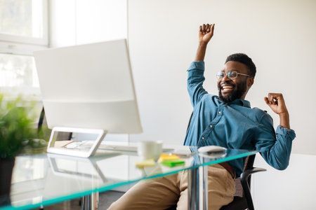 Man with glasses celebrates at a desk, raising arm in excitement.