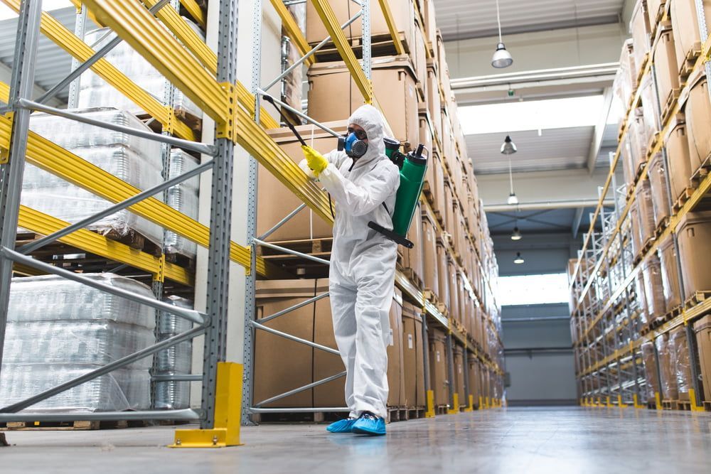 A Man In A Protective Suit Is Spraying A Warehouse With A Sprayer — Aust Outback Pest Co In Howard Springs, NT
