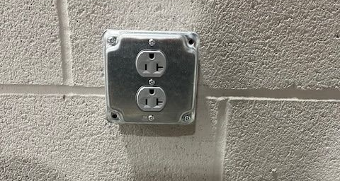 Metal electrical outlet box on a textured concrete block wall.