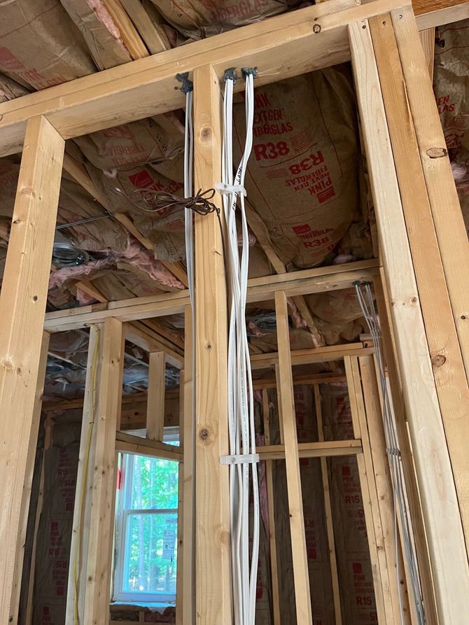 Interior view of a wooden framed wall with electrical wiring. Wires are bundled together and run vertically.