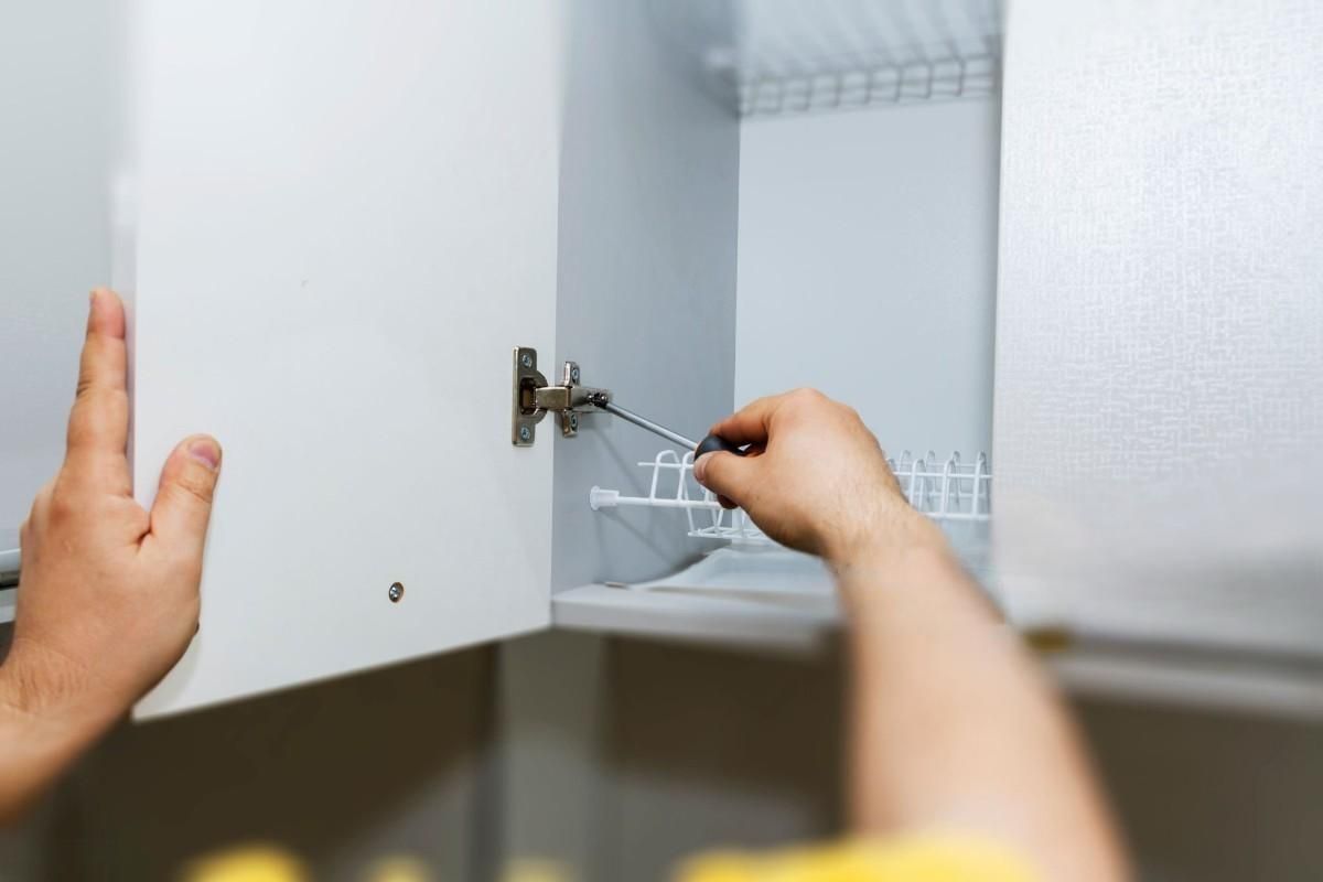A person is fixing a cabinet door with a screwdriver.