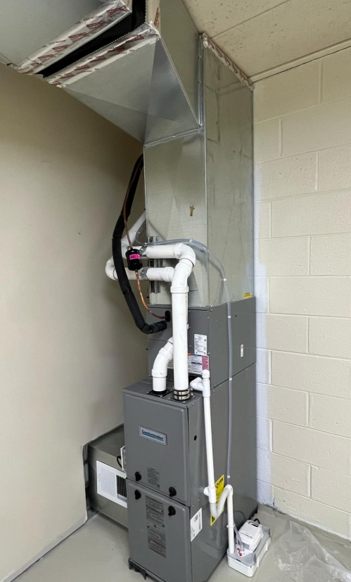 A high-efficiency gas furnace and AC coil unit installed indoors against a beige wall and white cinderblock corner.