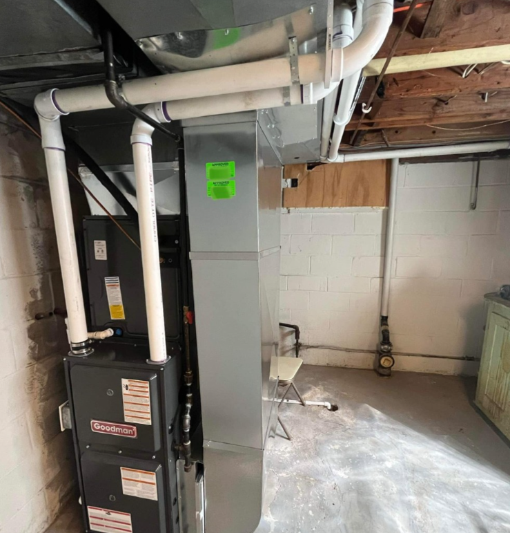 A dark gray Gradon furnace unit stands in a basement next to a tall, vertical metal ductwork system with white PVC piping.