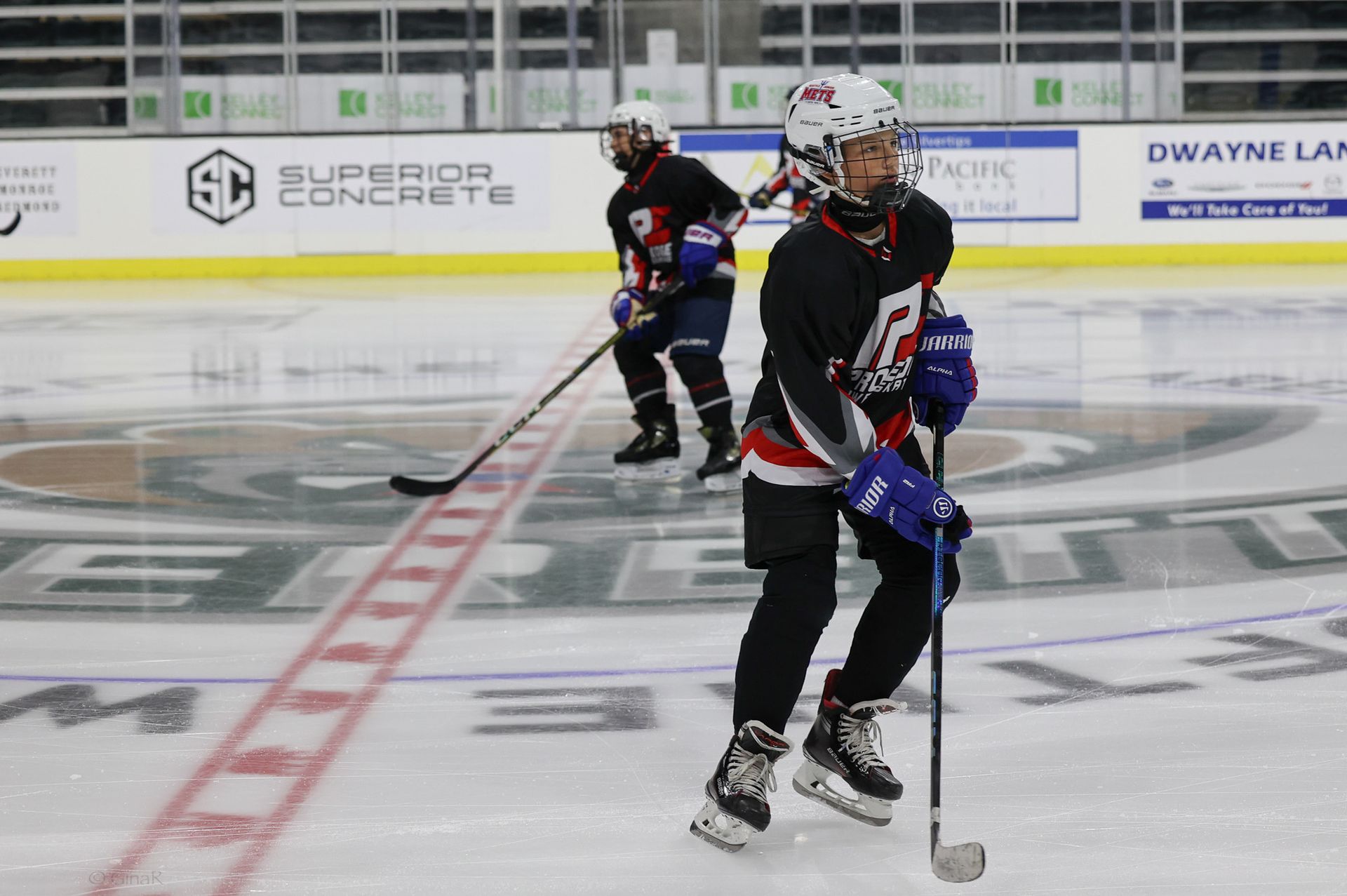 Two hockey players are playing on a rink with a superior concrete sign in the background