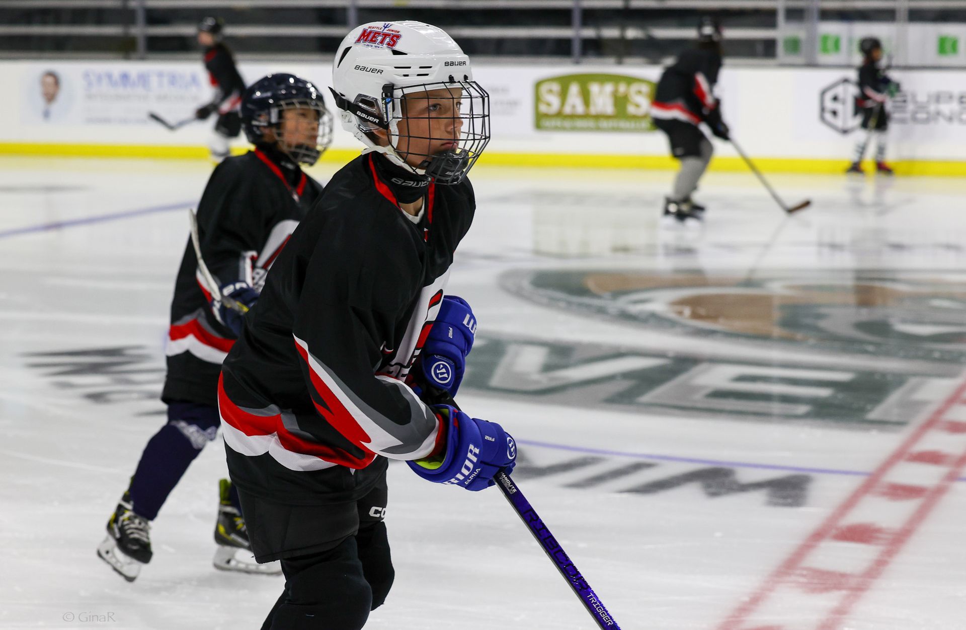 A group of young boys are playing ice hockey on a rink sponsored by sam 's