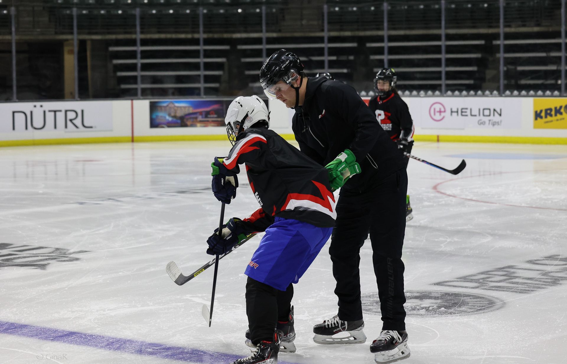 A man is helping a young hockey player on the ice