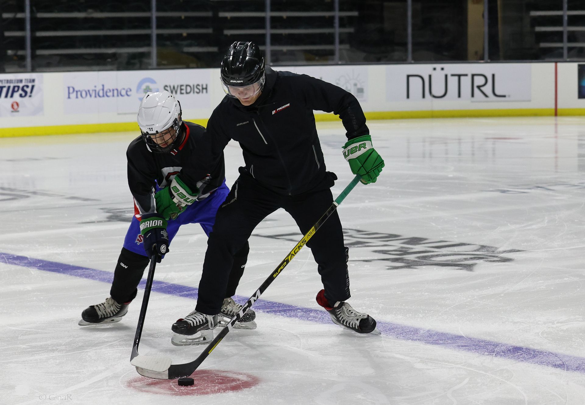 Two hockey players are playing on a rink with a nutrl sign in the background