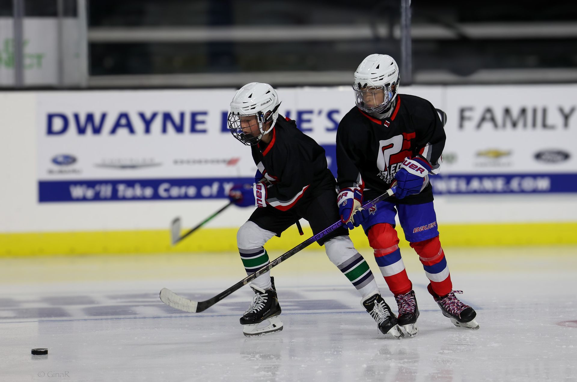 Two young boys are playing ice hockey on a rink sponsored by dwayne 's family.