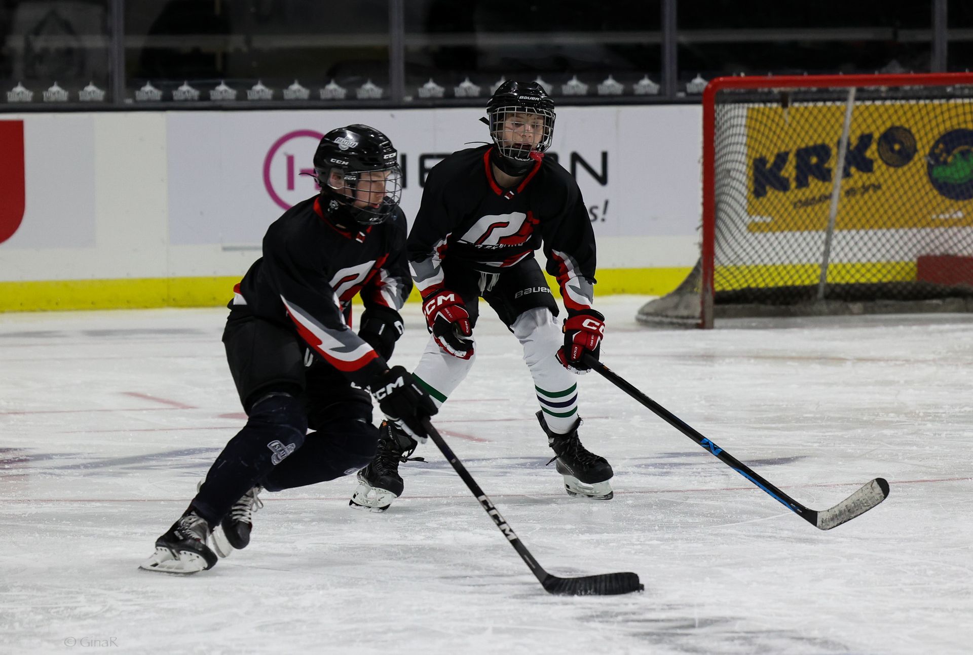 Two hockey players are playing on a rink with a krko sign in the background