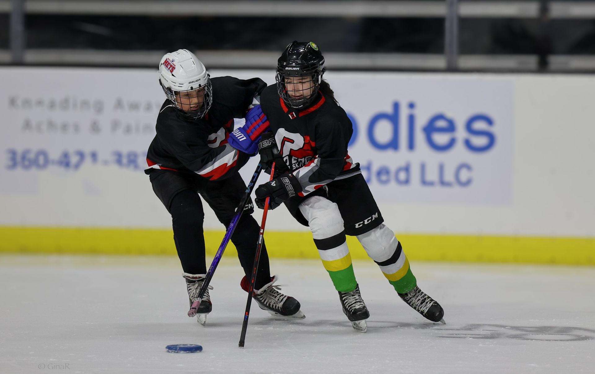 A hockey game is being played in front of a sign for bodies llc