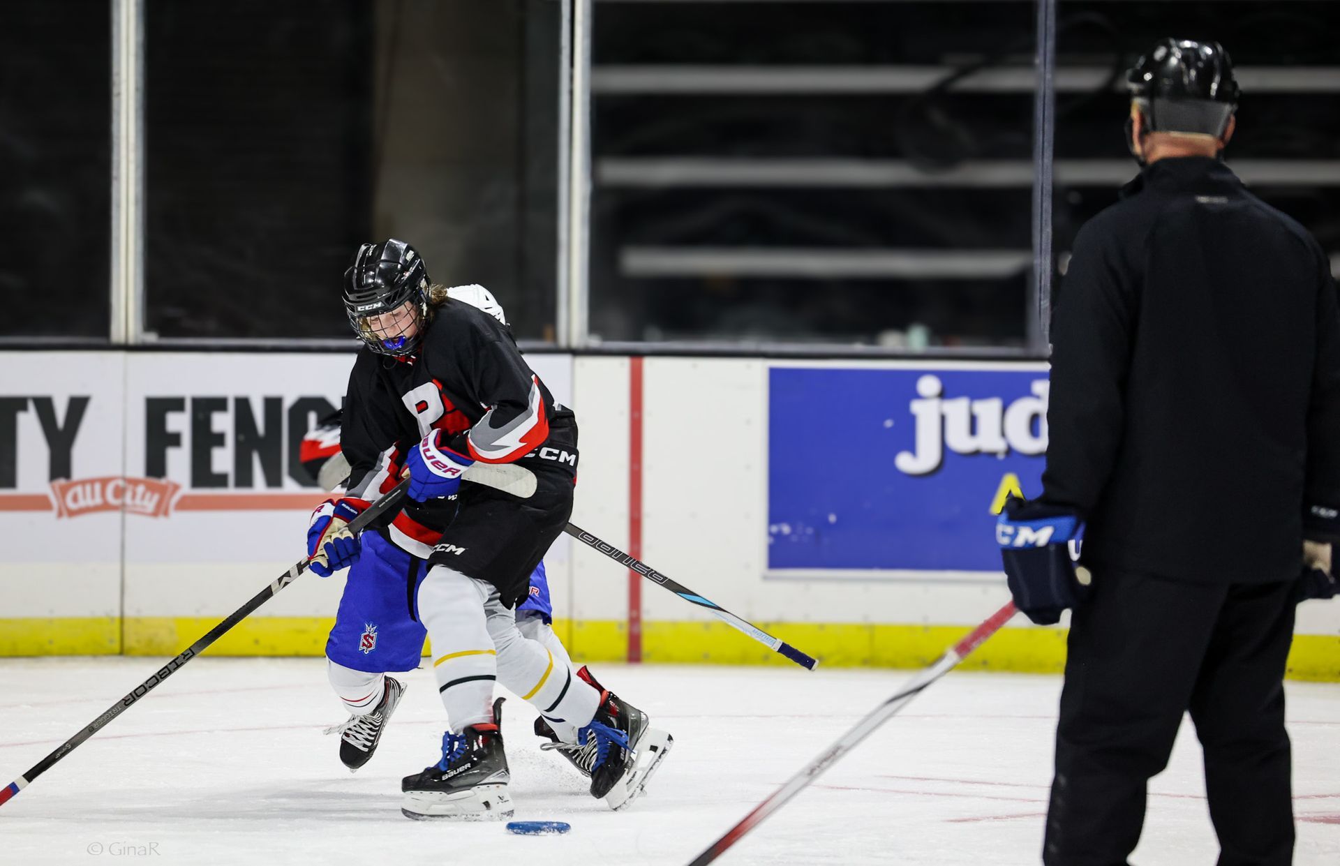 A hockey player is skating on the ice while a referee watches