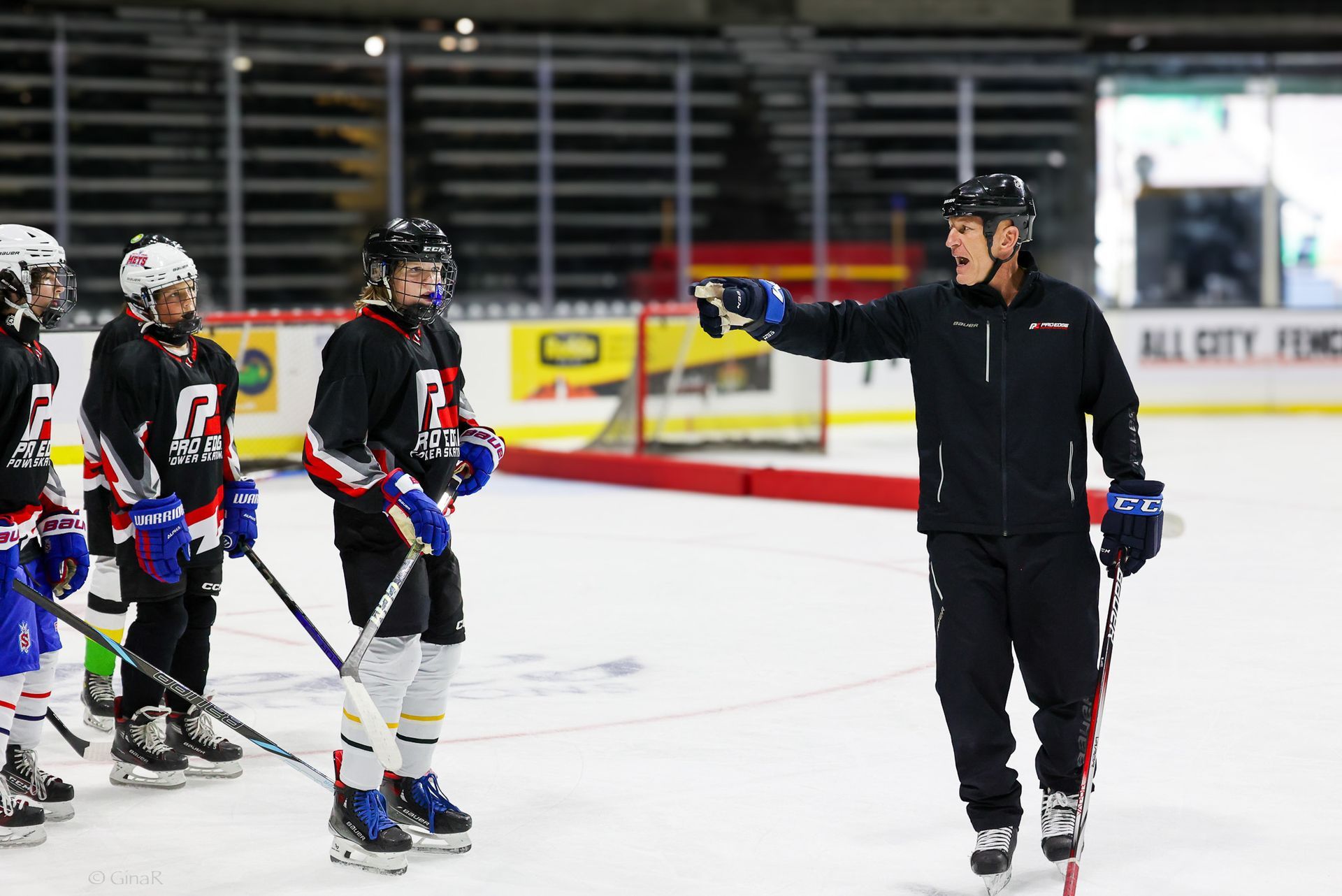 A man is standing on a hockey rink talking to a group of hockey players.
