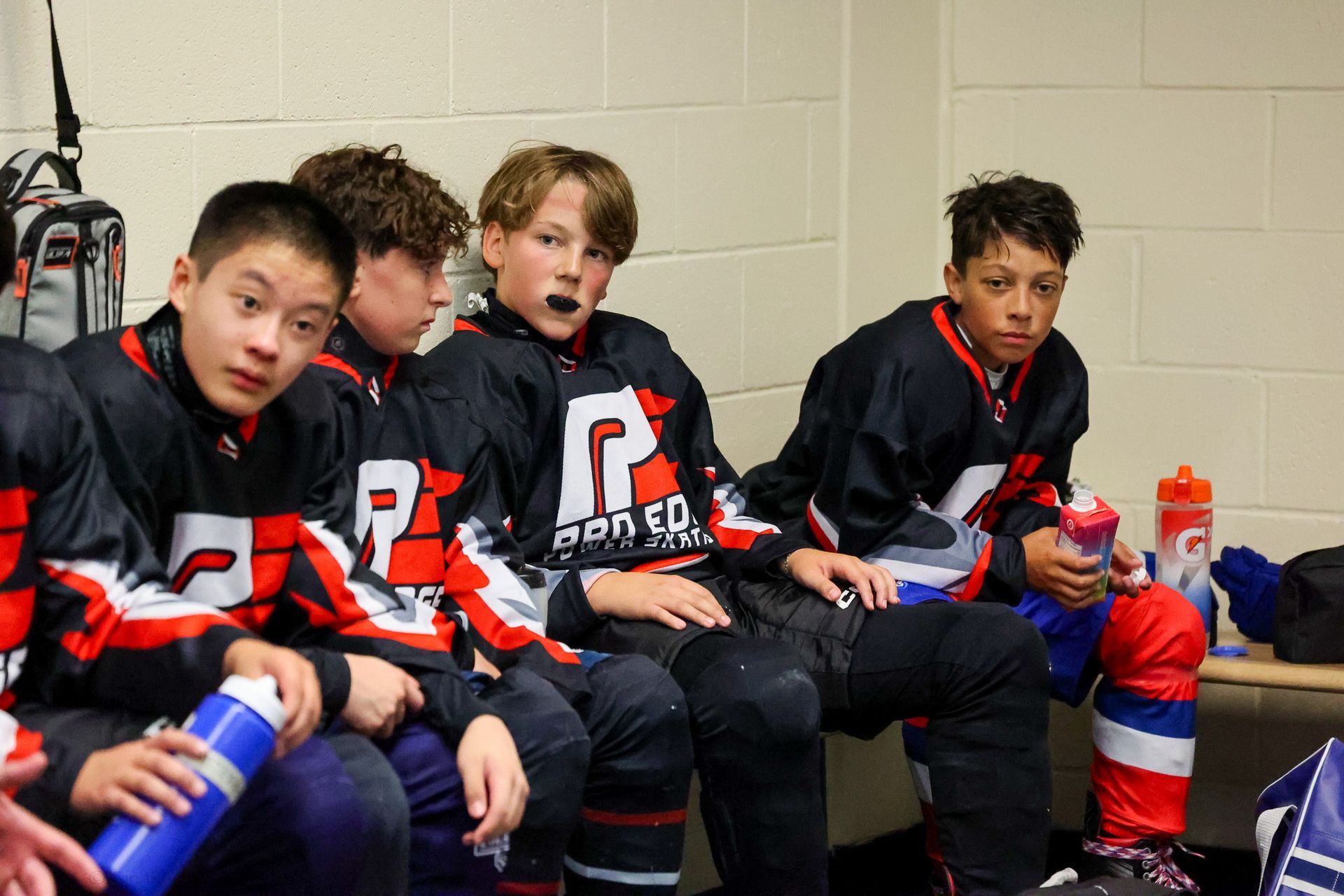A group of young boys are sitting on a bench in a locker room.