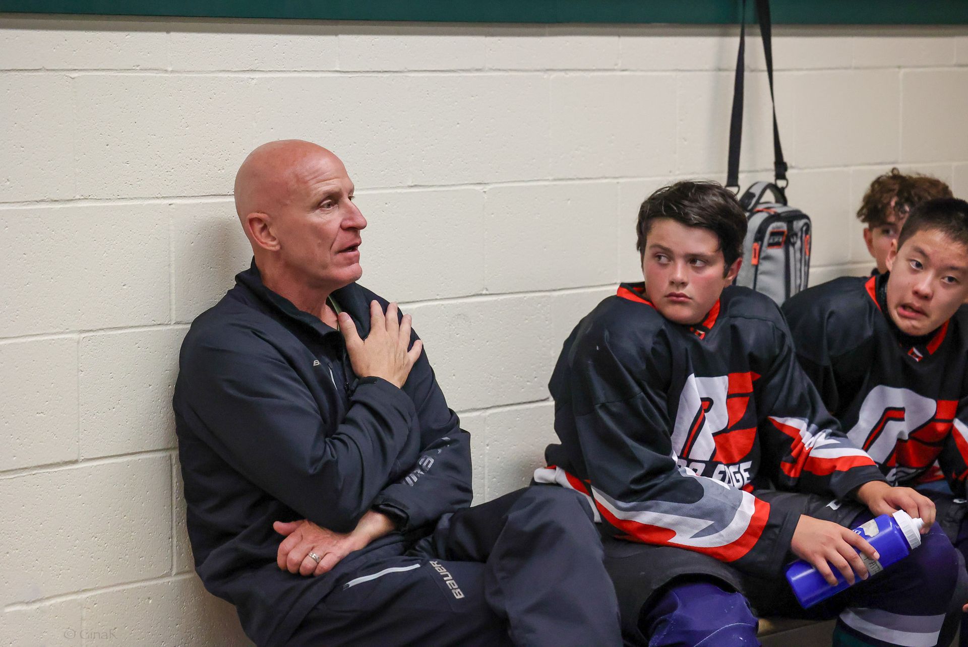 A group of hockey players are sitting in a locker room talking to their coach.