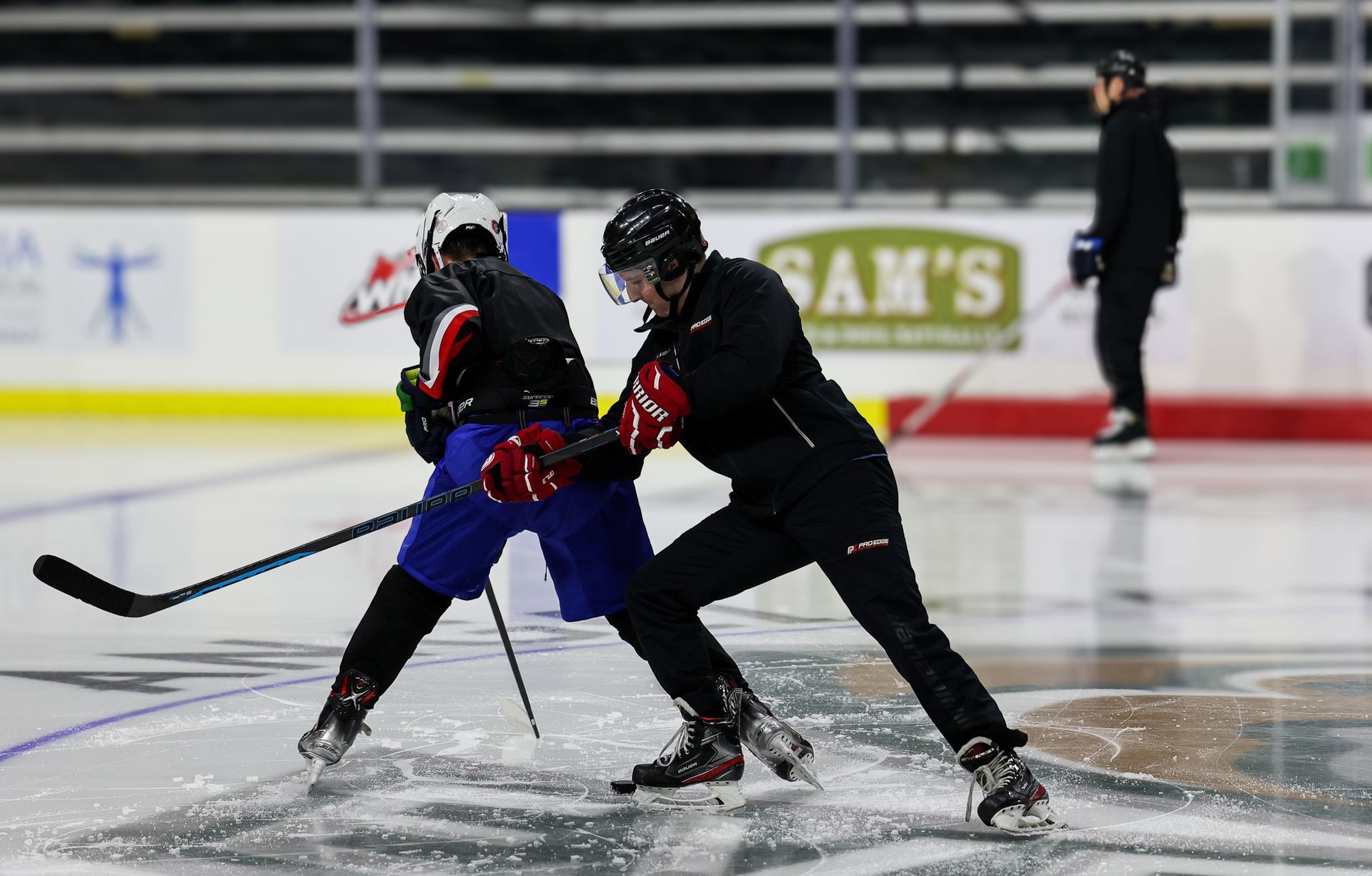 Two men are playing ice hockey on a rink with a sam 's sign in the background.
