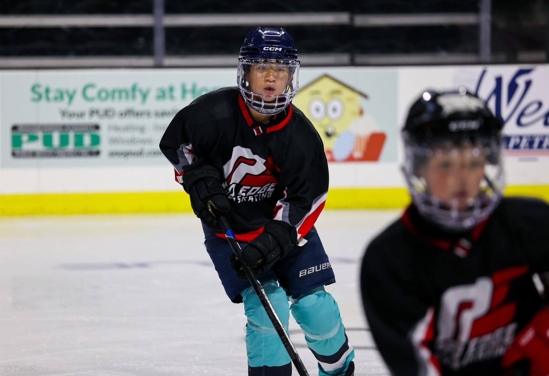 A hockey player with a stick on the ice with a sign in the background that says stay comfy at home