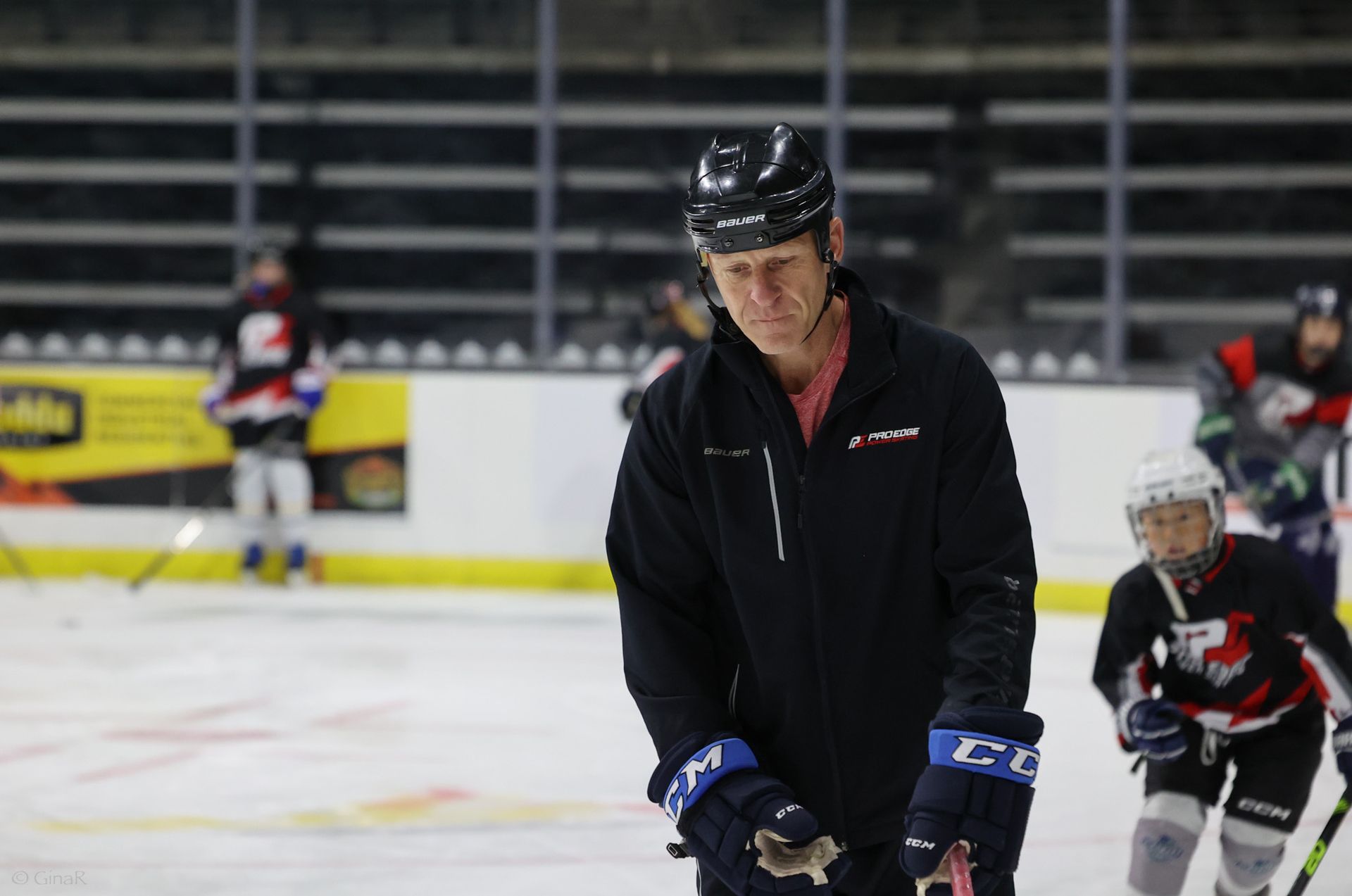 A man is standing on a hockey rink holding a hockey stick.