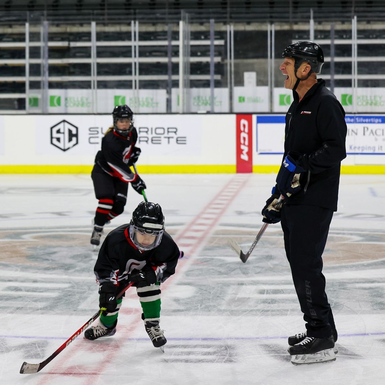 A man stands on a hockey rink talking to a young hockey player