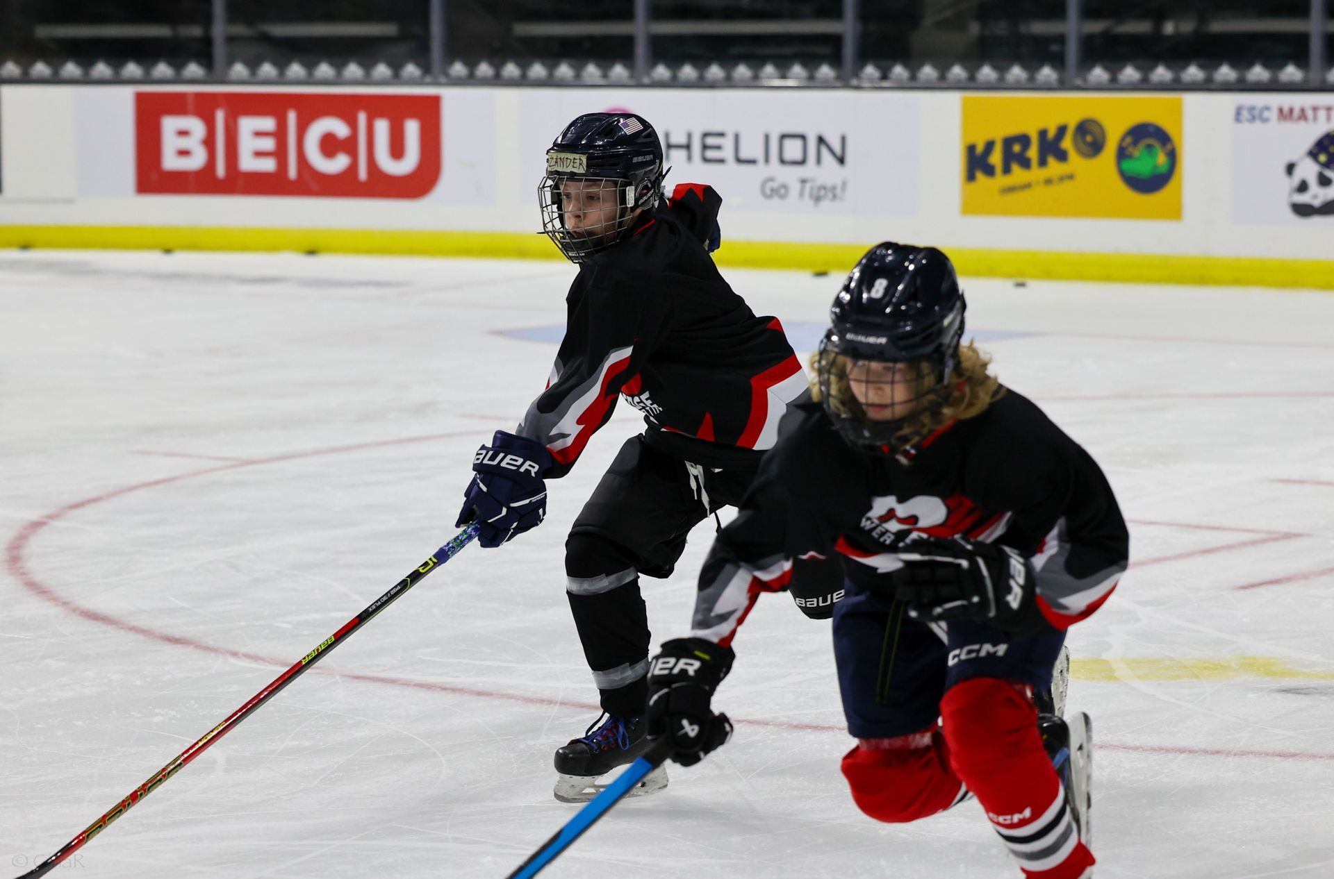Two young boys are playing ice hockey on a rink sponsored by helion and krk