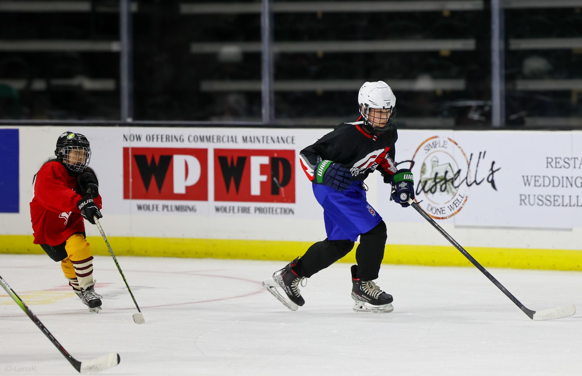 Two young boys are playing ice hockey on a rink sponsored by wpwf