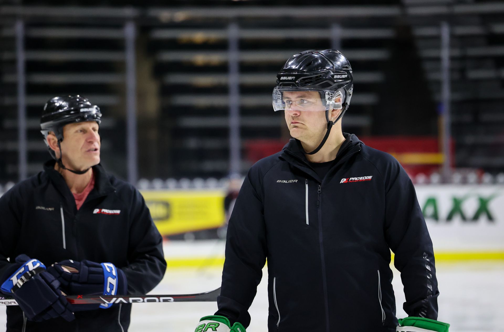 Two men are standing on a ice rink holding hockey sticks.