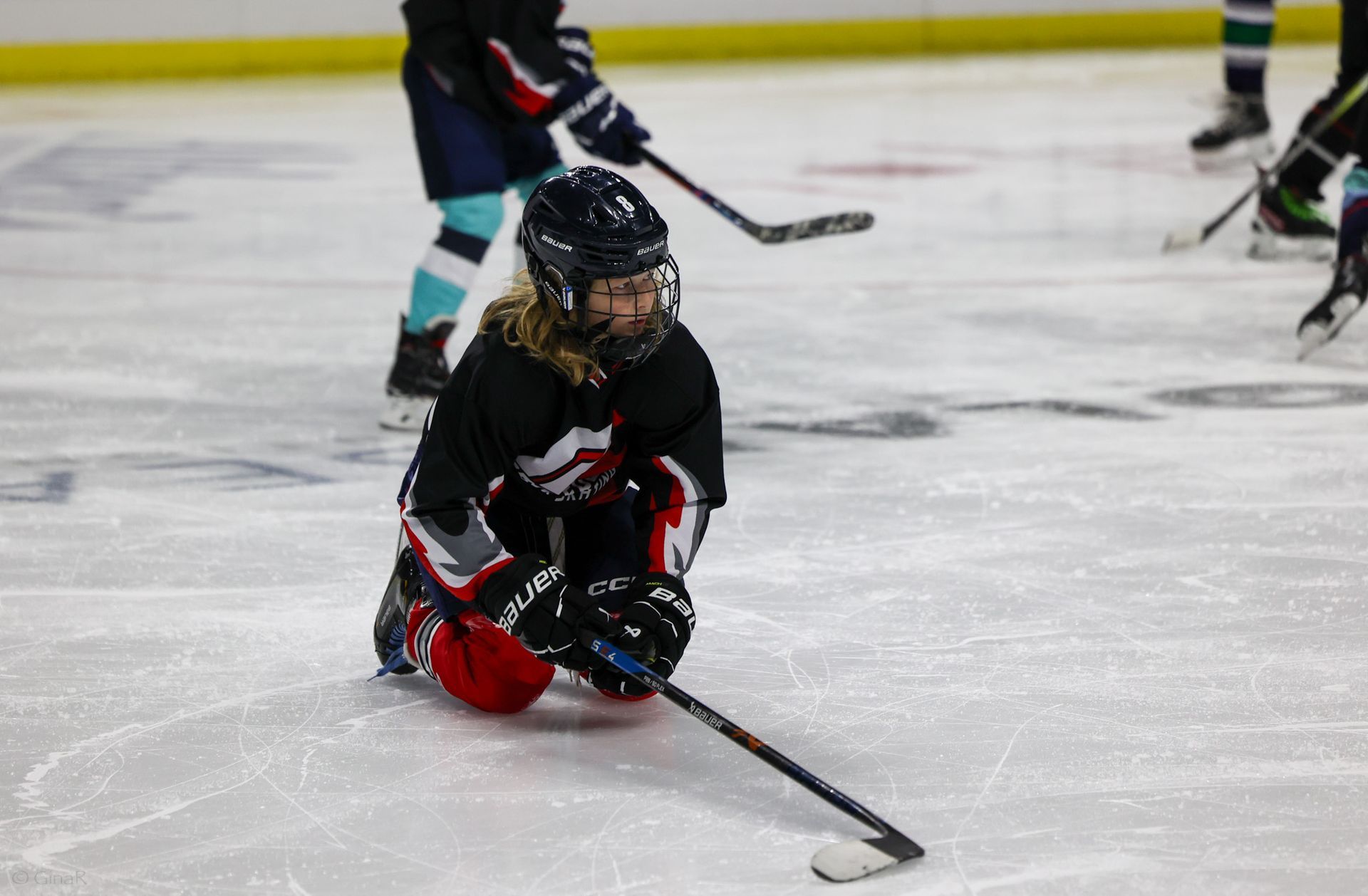 A young girl is kneeling on the ice holding a hockey stick.