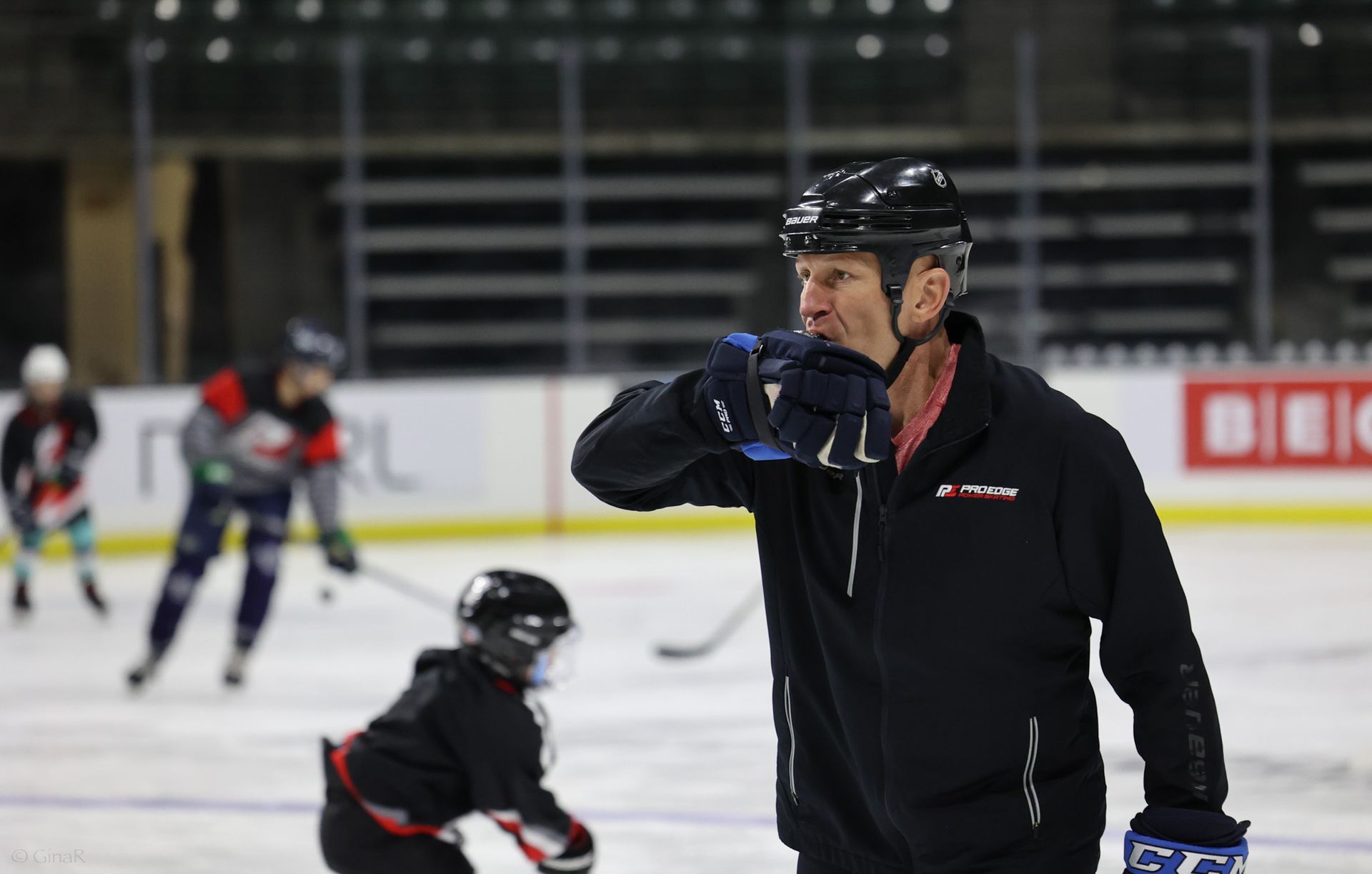 A man is standing on a ice rink talking to a hockey player.