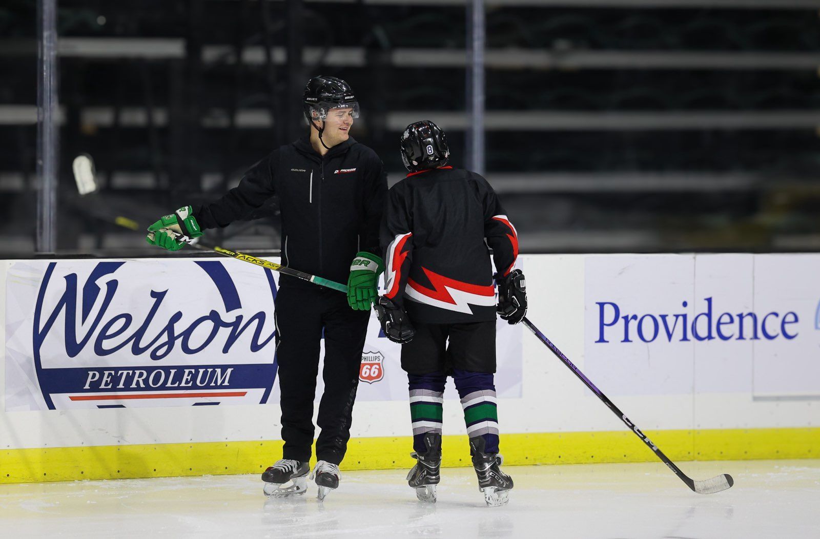 Two ice hockey players are standing on the ice talking to each other.