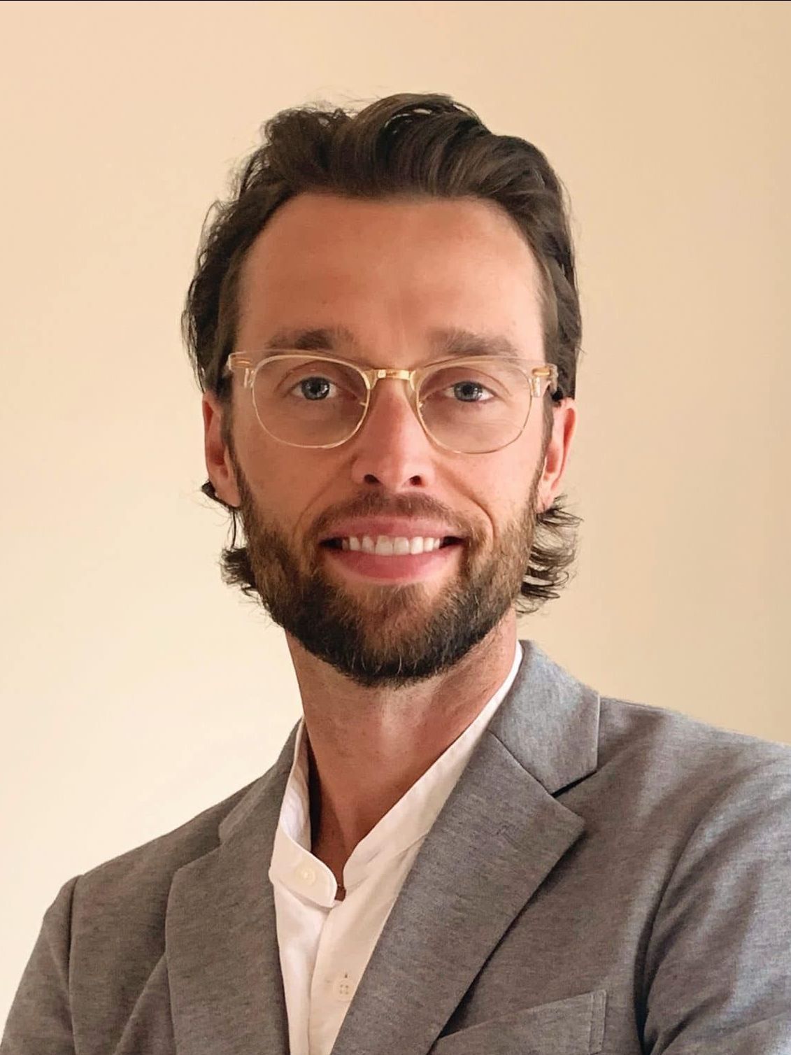 A man with a beard wearing glasses and a suit is smiling for the camera.