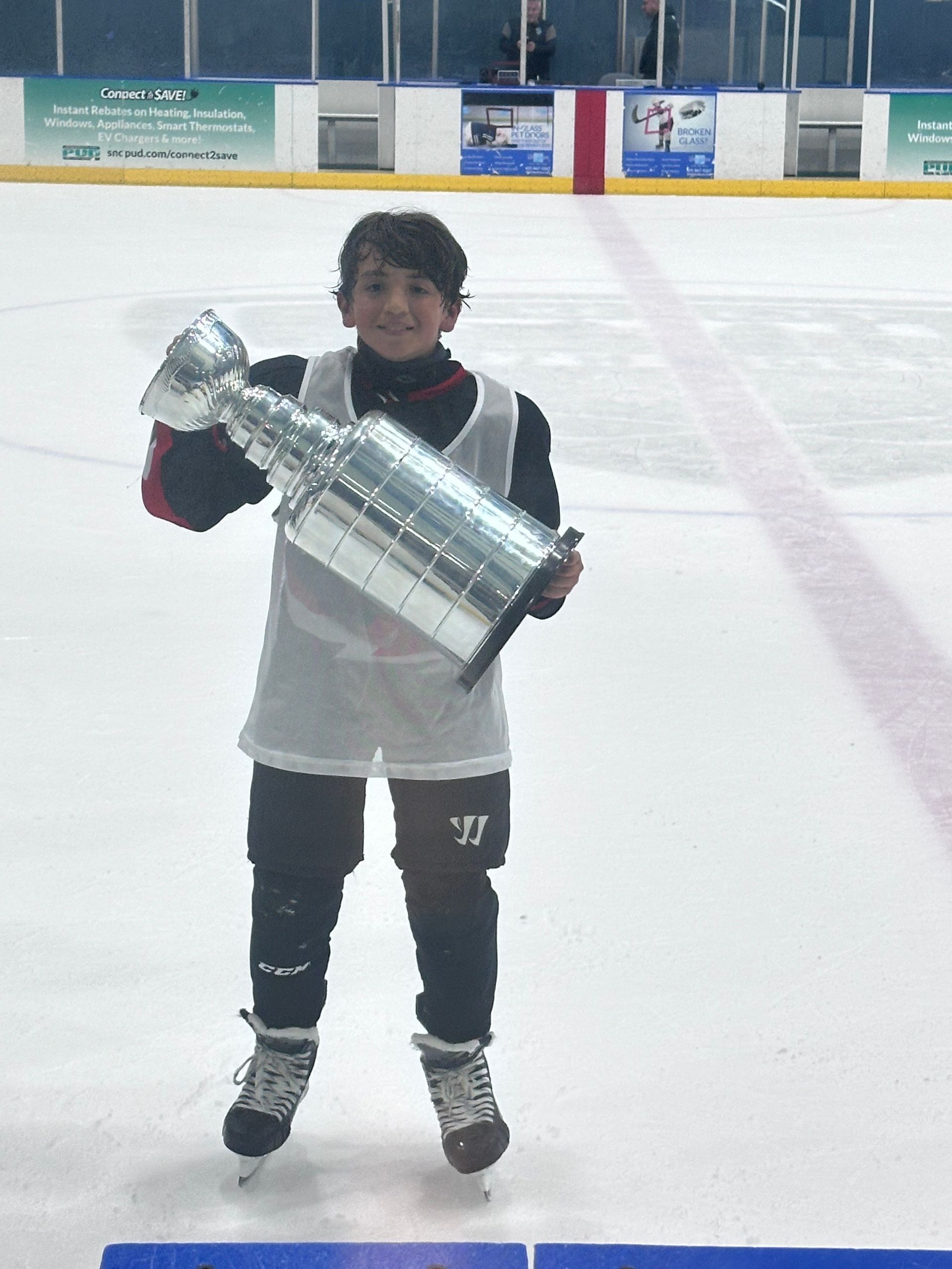 A hockey player is holding a trophy on the ice