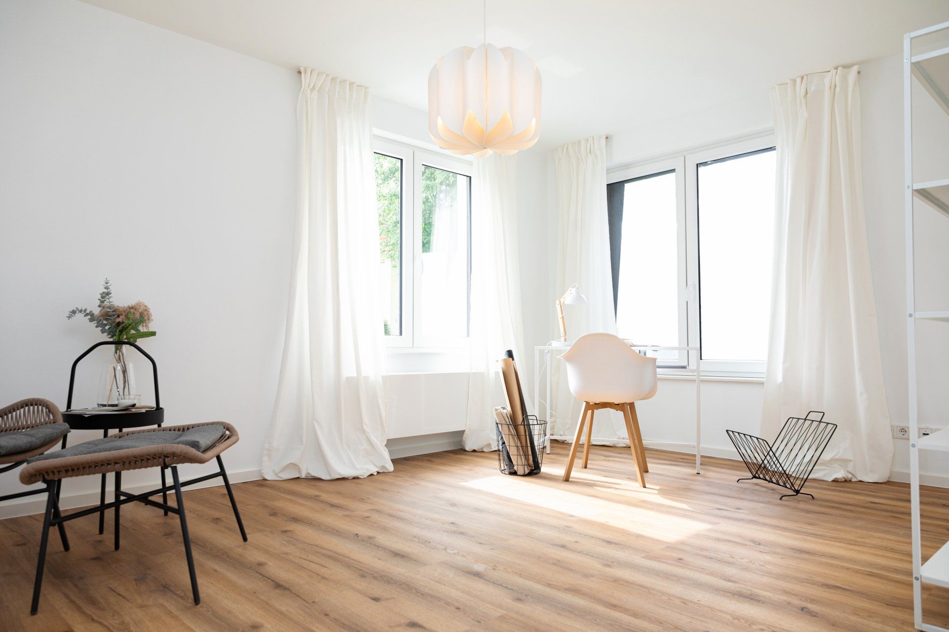 Ein Wohnzimmer mit Holzboden, weißen Vorhängen, einem Stuhl und einem Tisch.