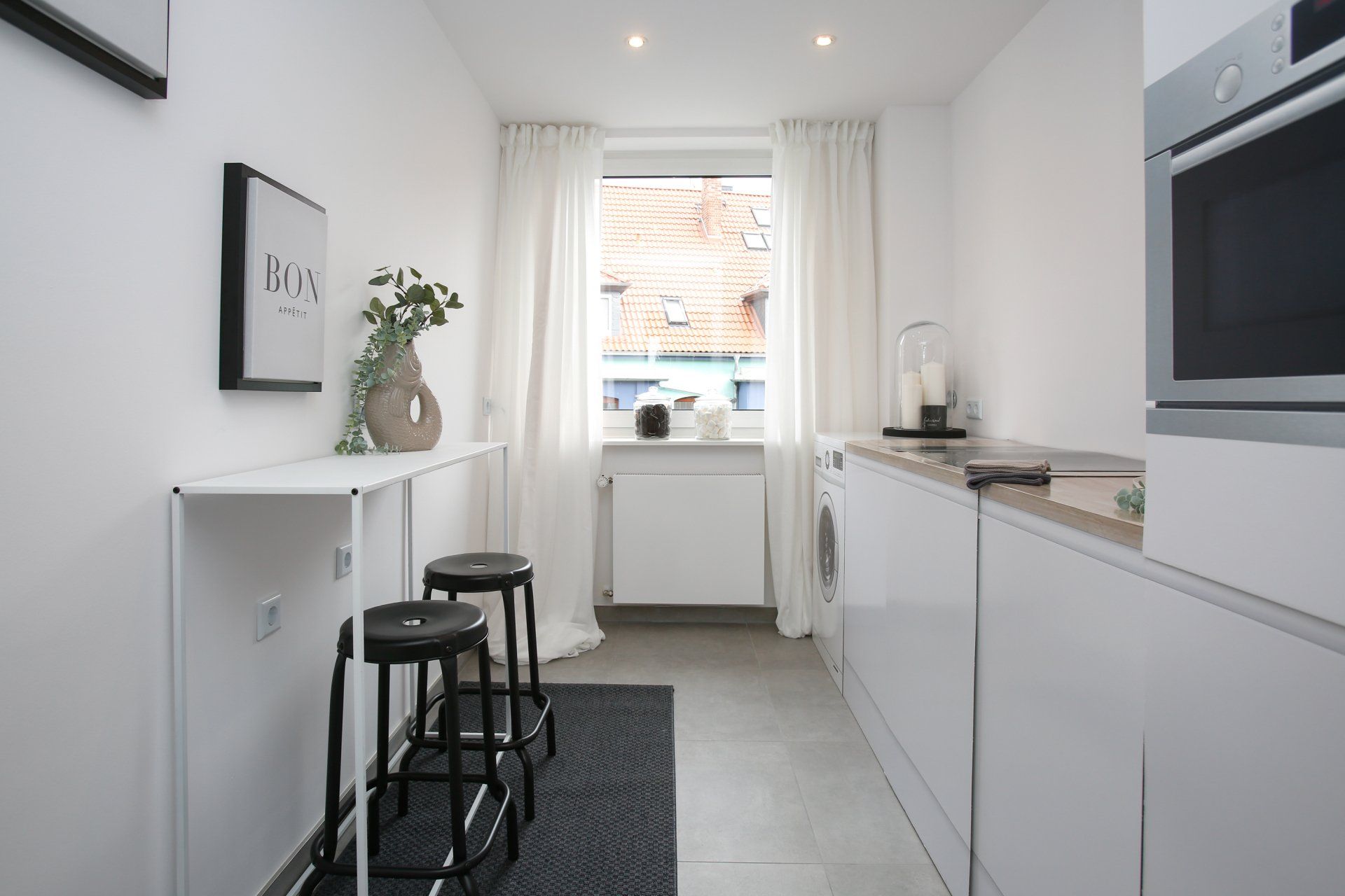 Eine Küche mit weißen Schränken und schwarzen Hockern und einem Fenster.