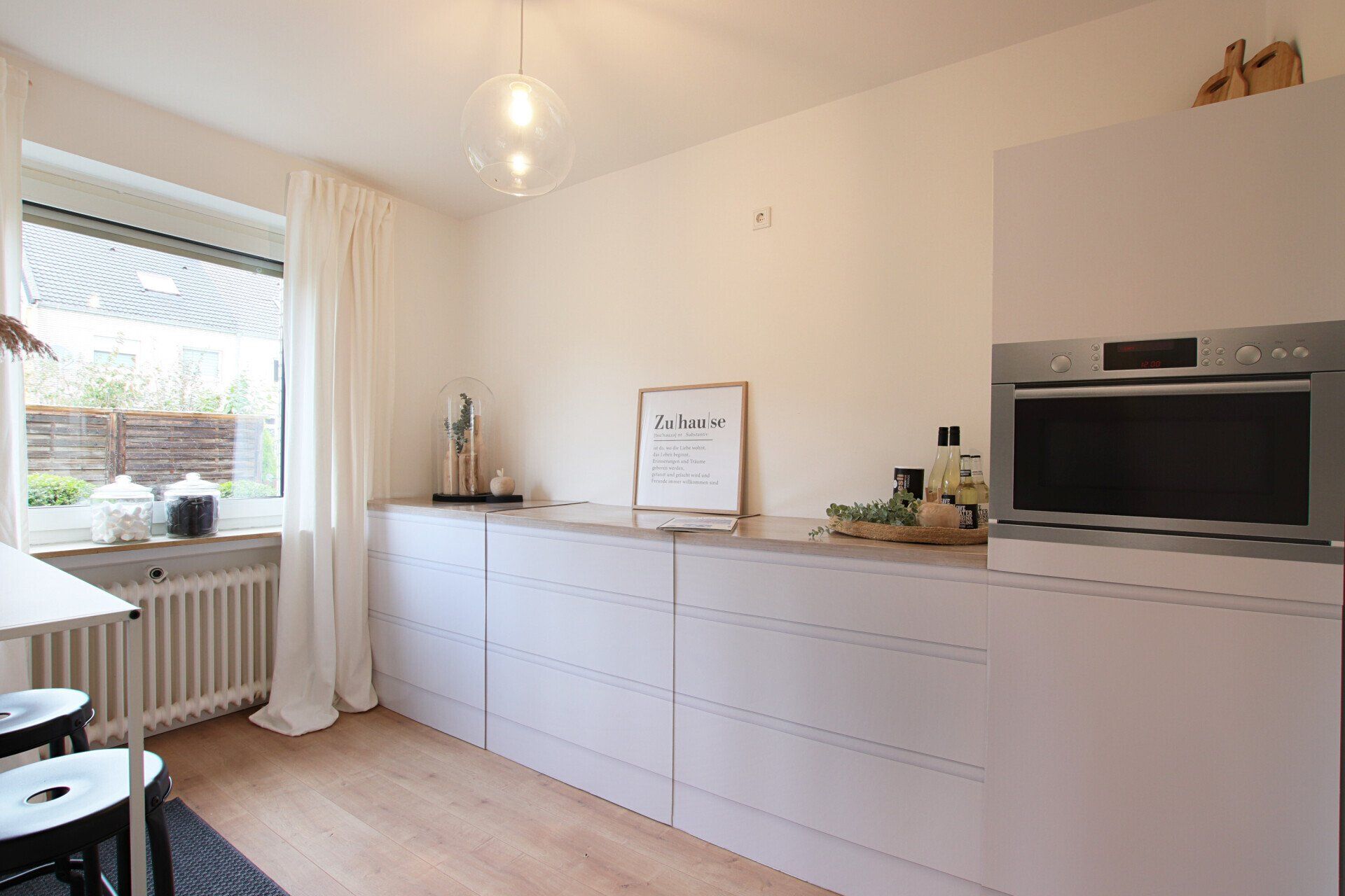 Eine Küche mit weißen Schränken, einer Mikrowelle und einem Fenster.