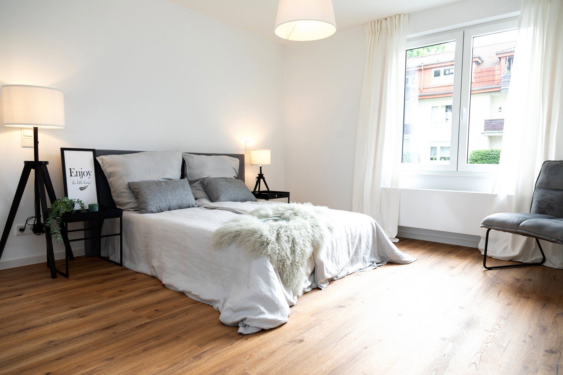 Ein Schlafzimmer mit Bett, Stuhl, Lampen und Fenster.