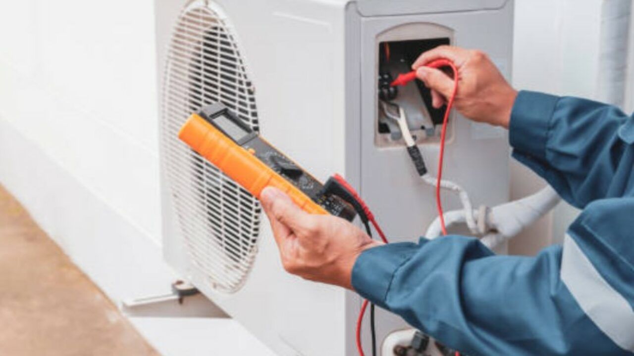 A man is working on an air conditioner with a multimeter.