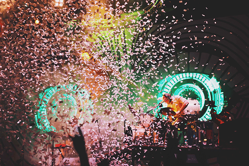 A group of people are playing instruments on a stage with confetti falling from the ceiling.