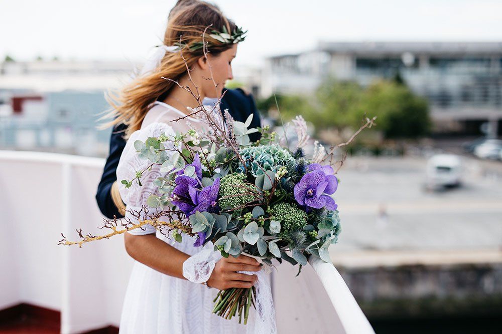 A bride and groom are standing on a balcony holding a bouquet of purple flowers.