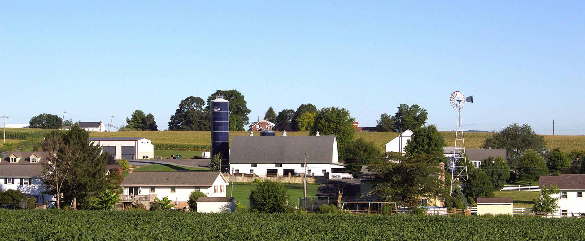Farm with white barn, silos, and green fields under a cloudy sky.