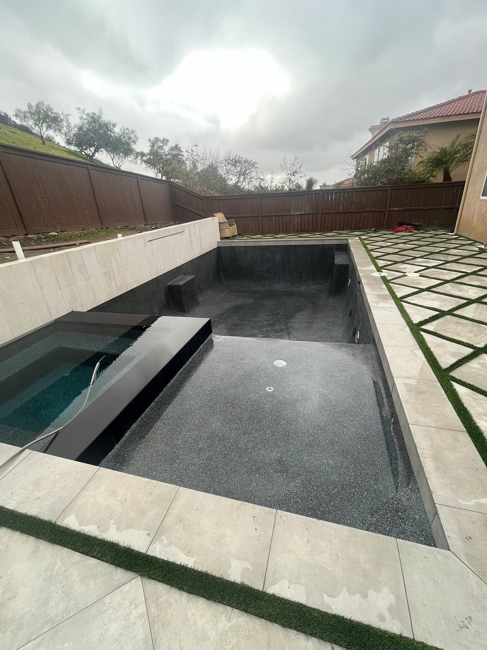 A large swimming pool is surrounded by a fence and a patio.