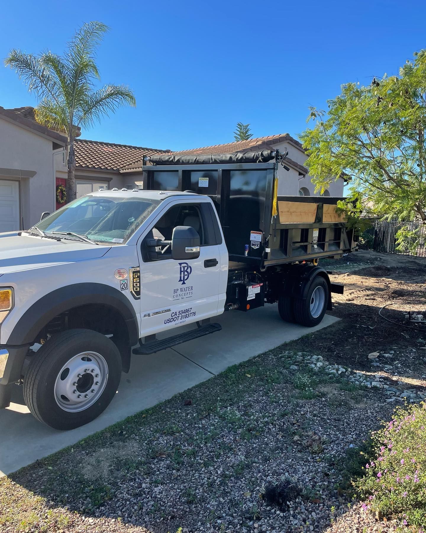 A white dump truck is parked on the side of the road in front of a house.